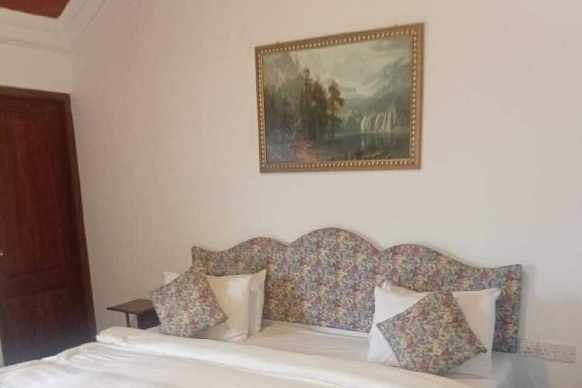 A bedroom with a floral-patterned bedspread, a wooden headboard, and a framed painting on the wall.