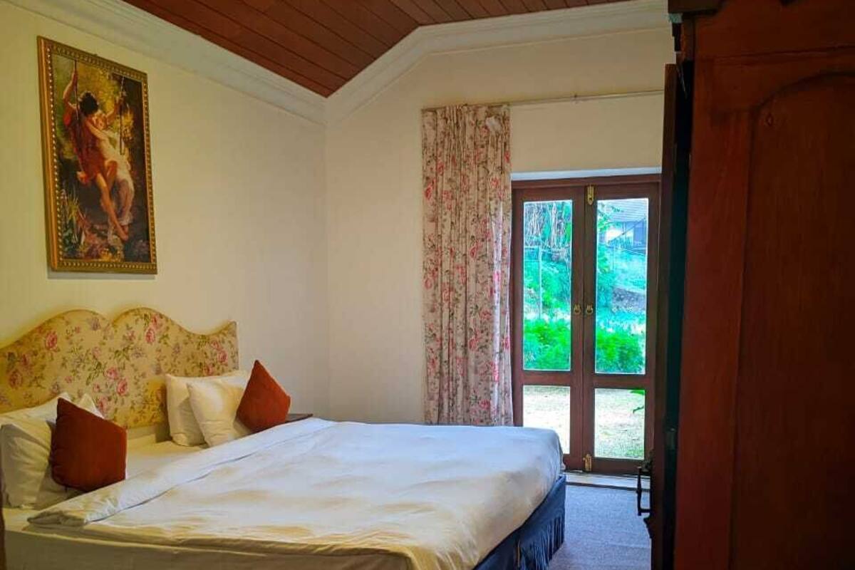 A bedroom with a bed, a painting, a door leading outside, and a carpeted floor.