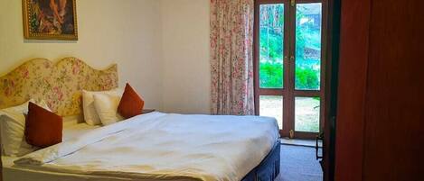 A bedroom with a bed, a painting, a door leading outside, and a carpeted floor.