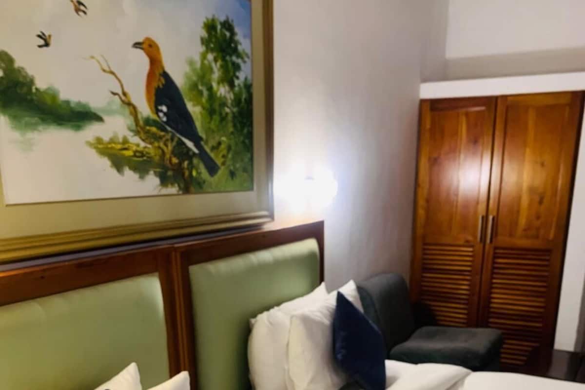 A hotel room with a bed, pillows, a headboard, a painting, and a wardrobe.