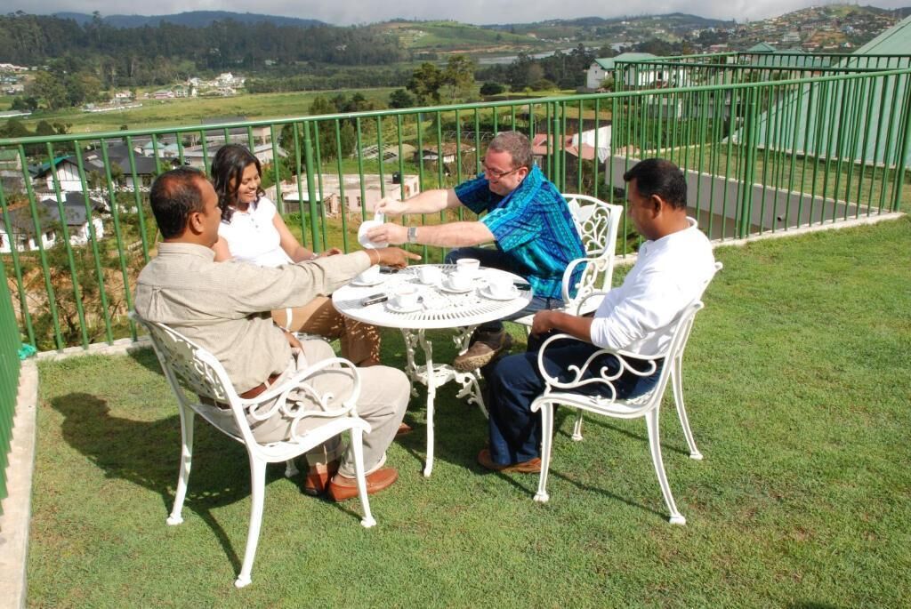 A group of people seated around a table on a balcony with a view of a green landscape.