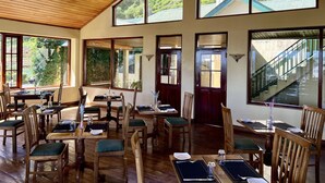 Comedor con mobiliario de madera y ventanas amplias que ofrecen vistas a zonas verdes y un edificio con techo verde.