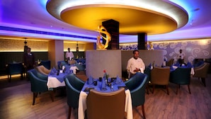 A restaurant with round tables, blue chairs, and a modern ceiling design. - Hotel Swosti Grand (Bhubaneshwar)