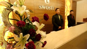 A reception desk with a floral arrangement and a sign reading "SWOSTI". - Hotel Swosti Grand (Bhubaneshwar)