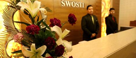 Un mostrador de recepción con un arreglo floral y un cartel que dice 'SWOSTI'.