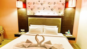 A hotel room with a neatly made bed, a heart-shaped towel arrangement, a telephone, a water bottle, and a nightstand with a lamp. - Hotel Swosti Grand (Bhubaneshwar)