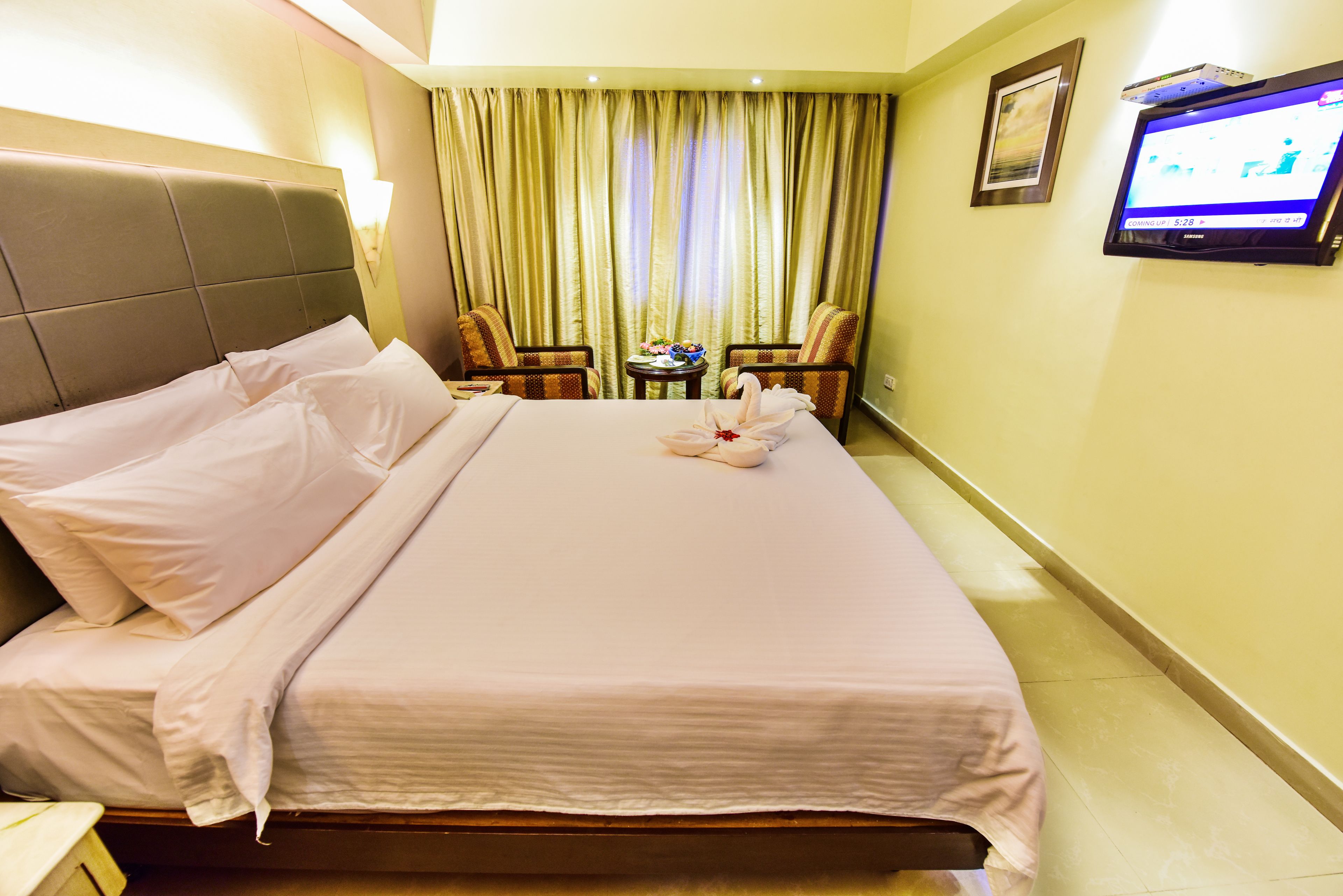A hotel room with a neatly made bed, a television on the wall, and a small table with a vase of flowers.