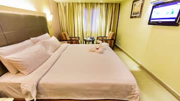 Ein Hotelzimmer mit einem ordentlich bezogenen Bett, einem an der Wand befestigten Fernseher und einem kleinen Tisch mit einer Blumenvase.