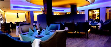 Un comedor moderno con mesas y sillas redondas, iluminación ambiental y vistas al área del bar.