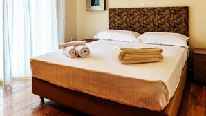 A hotel room with a large bed, two rolled towels, a patterned headboard, and a wooden floor.