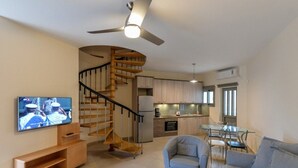 A modern living room with a TV, a sofa, a glass coffee table, and a staircase leading to a kitchen.