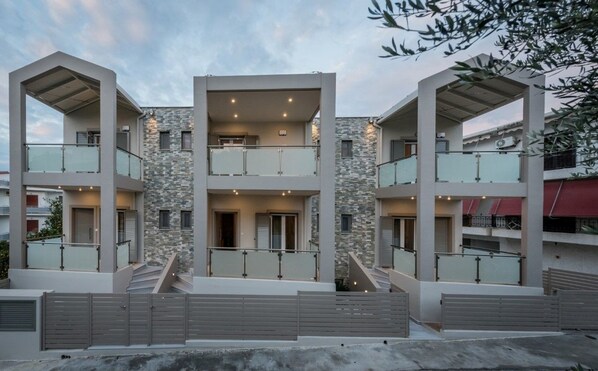 Un edificio moderno de varios pisos con balcones, fachada de piedra y entrada porticada.