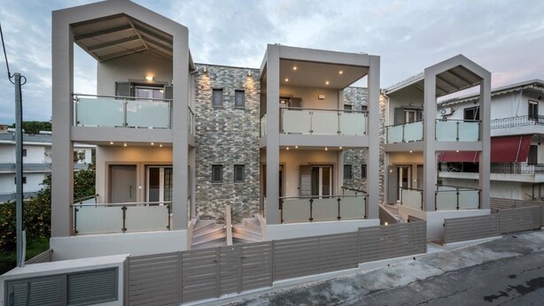 A modern multi-story residential building with balconies, a stone facade, and a gated entrance.