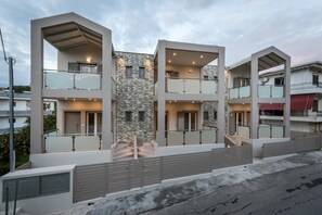 Un edificio residencial moderno de varios pisos con balcones, fachada de piedra y entrada protegida por un portón.