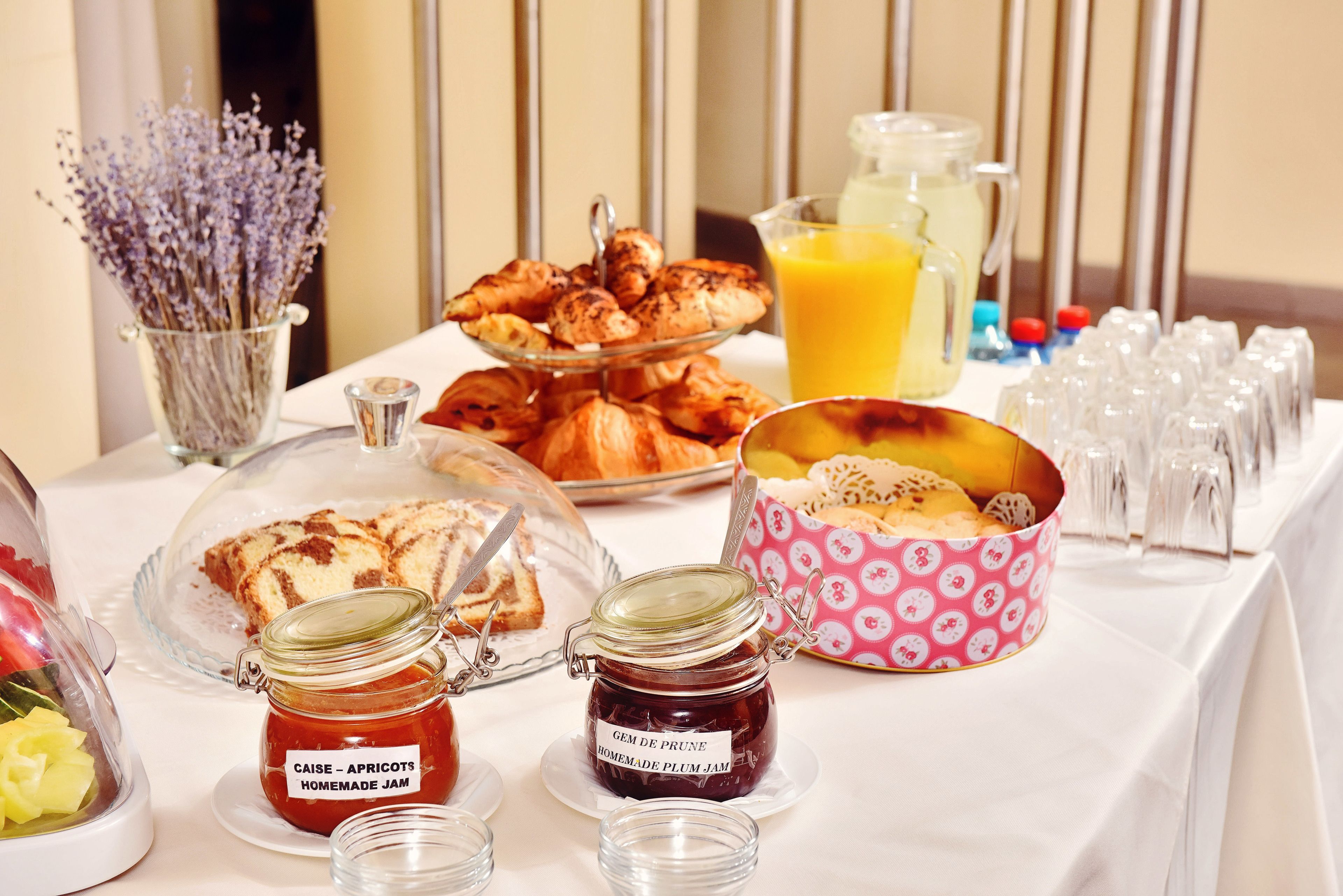 Un bufé de desayuno con diversos pasteles, mermeladas y un vaso de jugo de naranja.