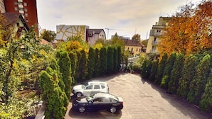 An outdoor patio area with tables and chairs, a parked car, and surrounding greenery. - President Hotel (Timisoara)