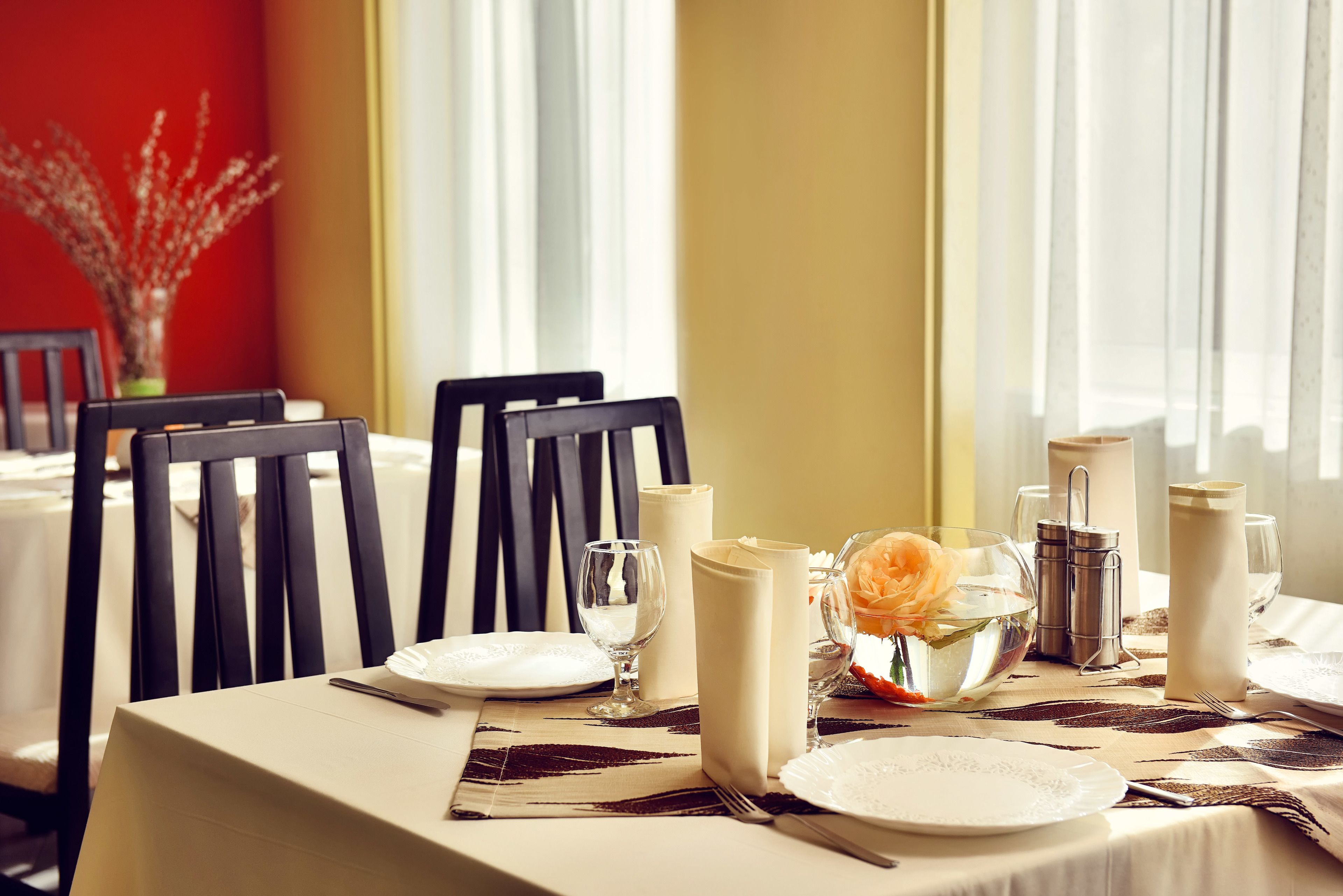 A dining table set with white plates, glasses, and a vase with flowers.