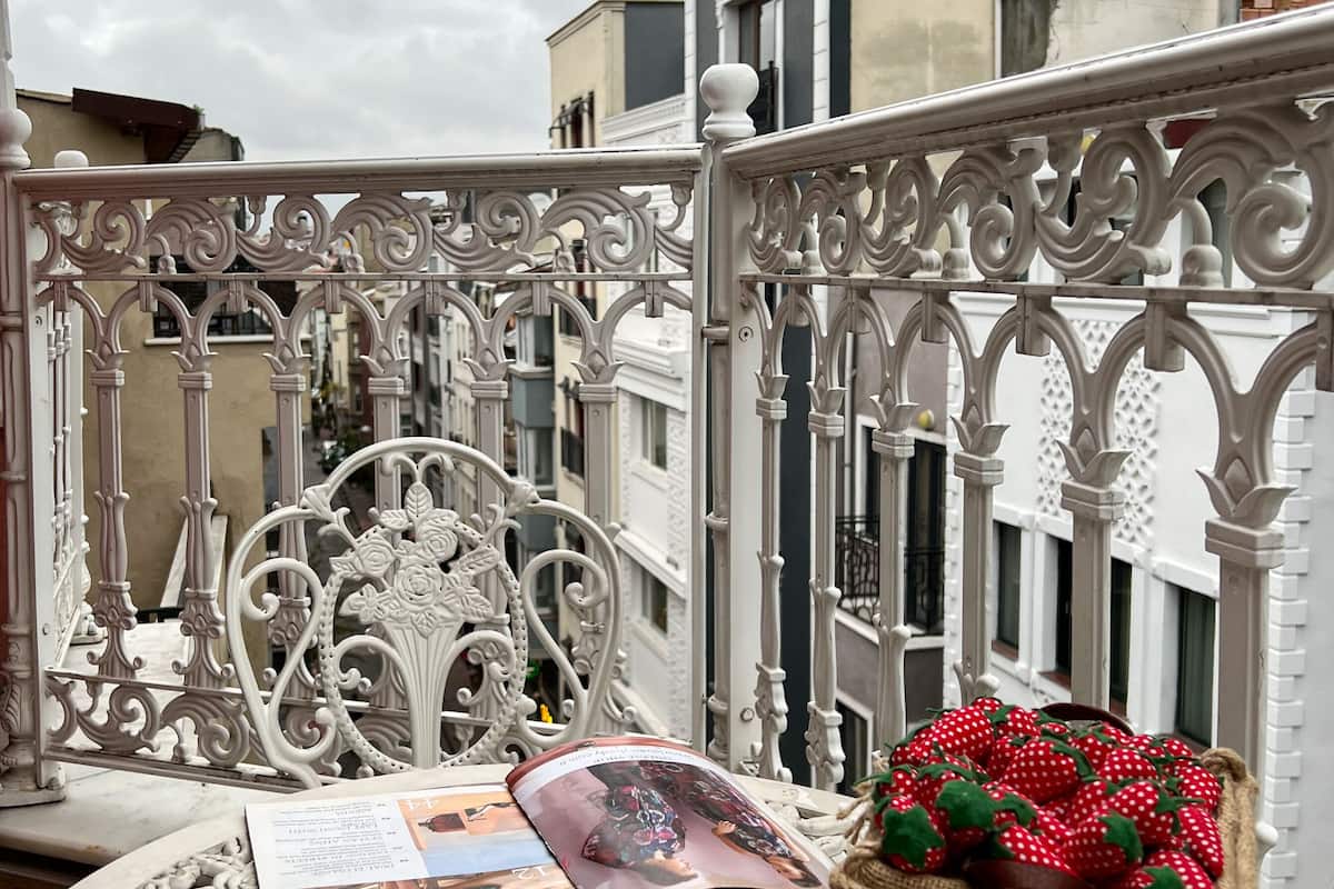A balcony with ornate white metal railings, a table with a cup of coffee, a plate of pastries, a basket of strawberries, and a magazine.