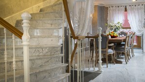 Eine Marmortreppe mit weißen Balustraden führt zu einem Essbereich mit einem Holztisch, gedeckt für vier Personen, umgeben von Stühlen.