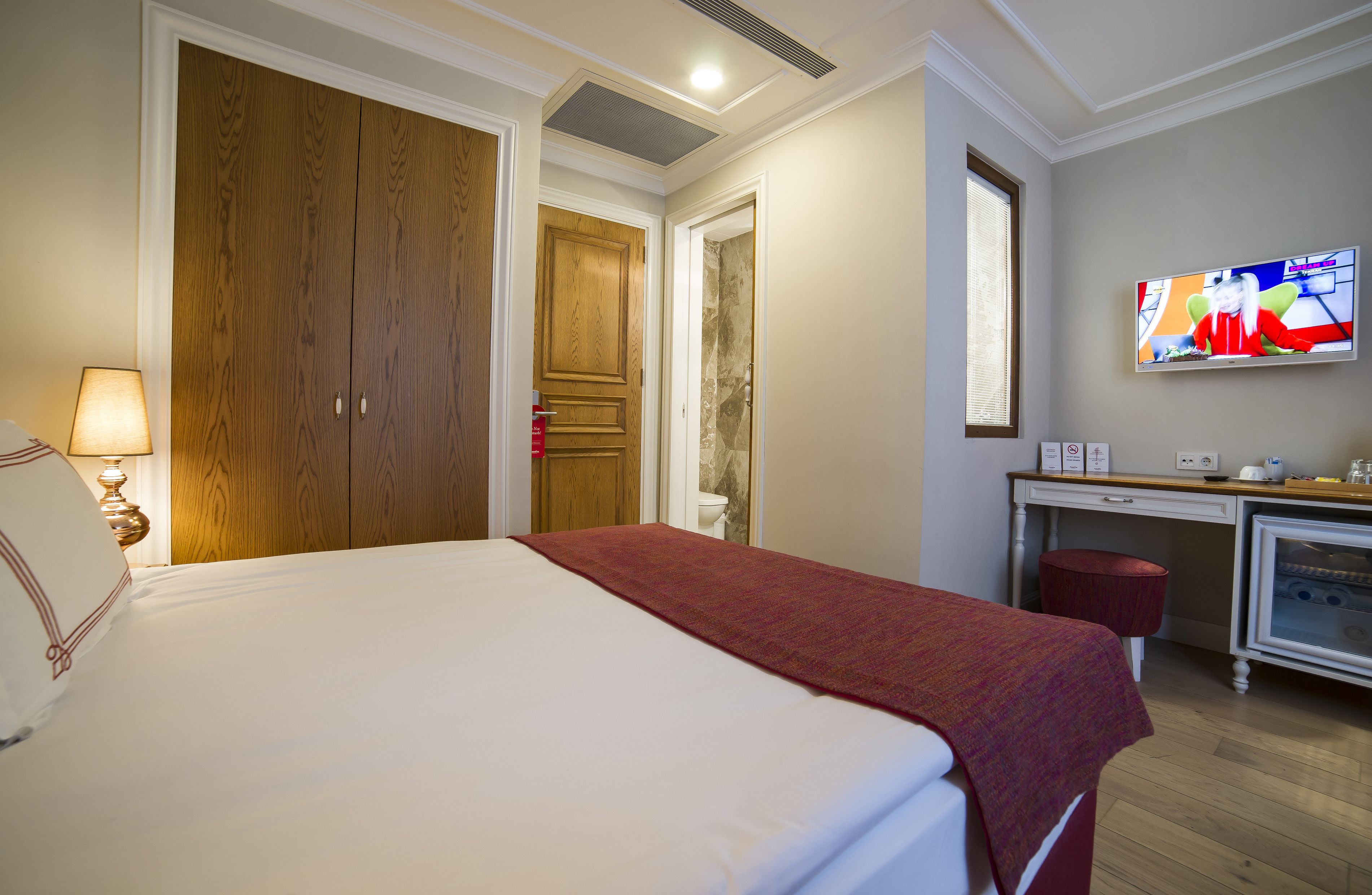 A hotel room with a large bed, a desk with a computer, a television, and a wardrobe.