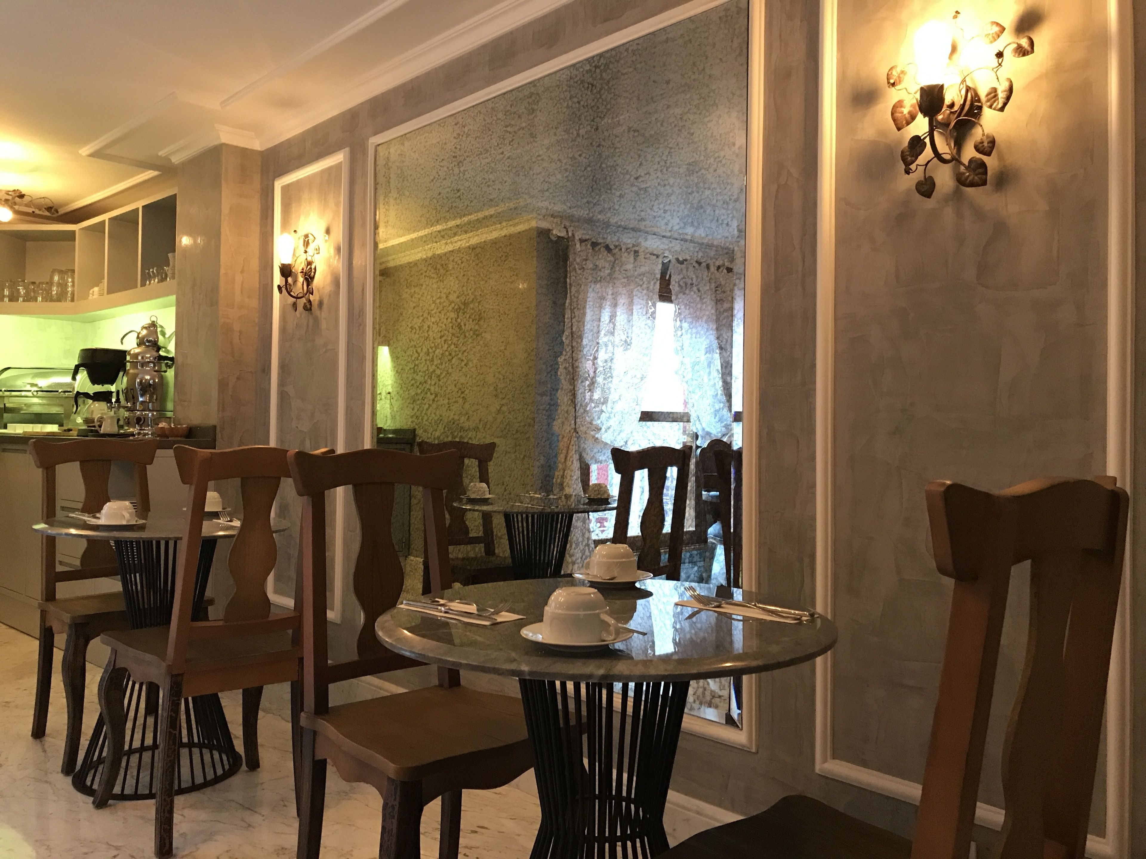 Un espace repas avec des tables rondes et des chaises en bois, une cuisine à l’arrière-plan et un grand miroir qui reflète la pièce.