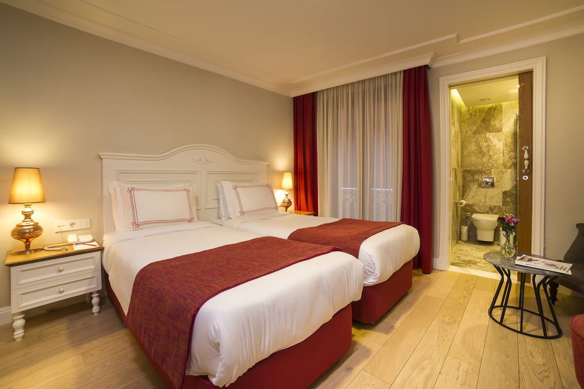 A hotel room with two beds, a nightstand, a table, and a bathroom visible through an open door.