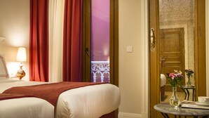 Ein Hotelzimmer mit zwei Betten, einem kleinen runden Tisch mit einer Blumenvase und einer Tür zu einem weiteren Raum.