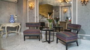 Ein modernes Wohnzimmer mit Marmorboden, einer Treppe und einem großen Spiegel, der den Raum reflektiert. Es sind vier Polsterstühle, ein kleiner Tisch und eine dekorative Vase zu sehen.