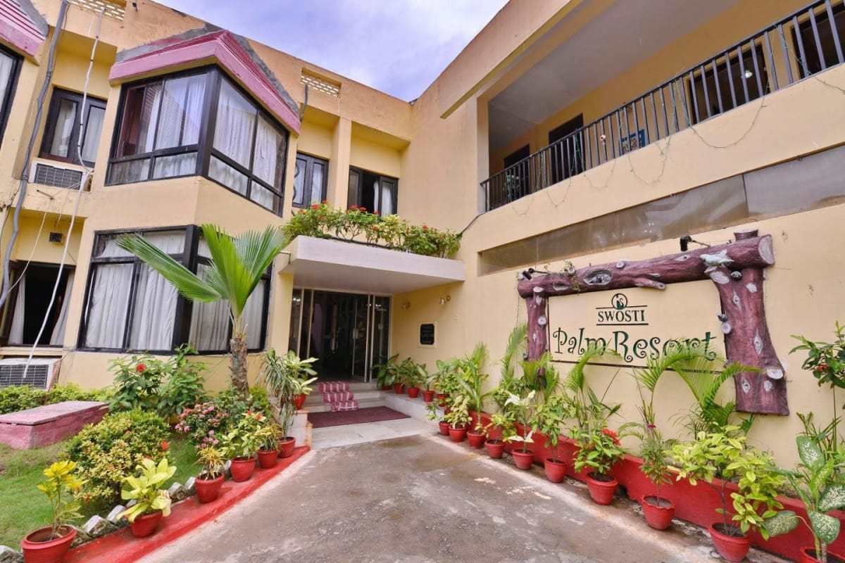 A building with a sign reading "SWOSTI Palm Resort," featuring a courtyard with potted plants and a red pathway.