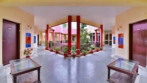 Un vestíbulo de hotel con una estructura central roja y blanca, mesas de vidrio y plantas en macetas.