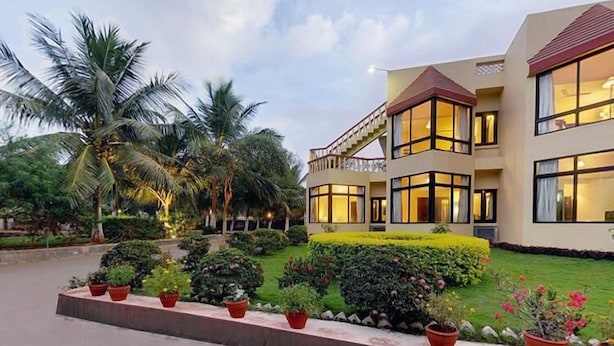 Un hotel moderno con una estructura de dos pisos, un balcón y un jardín bien cuidado con diversas plantas.