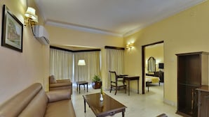 Habitación de hotel con un sofá de cuero marrón, una mesa de centro de madera, una mesa de comedor con sillas, un espejo grande y un armario.