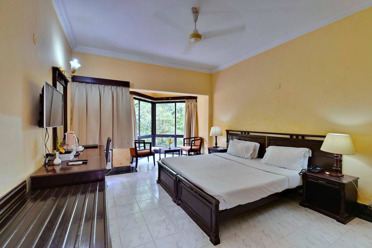 Une chambre d’hôtel avec un grand lit, un bureau avec une chaise, une télévision et une fenêtre avec des rideaux.