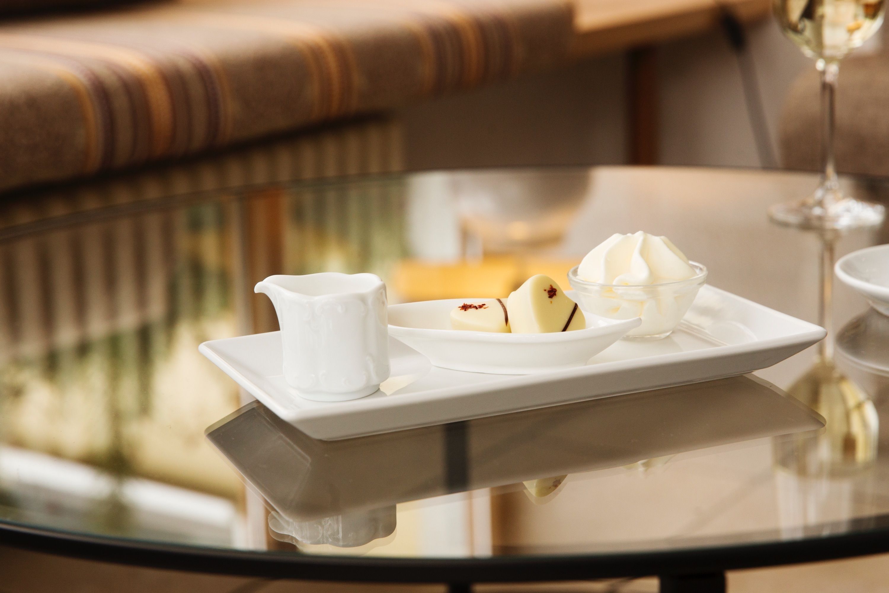 A dessert tray with a scoop of ice cream and a small pitcher on a glass table.