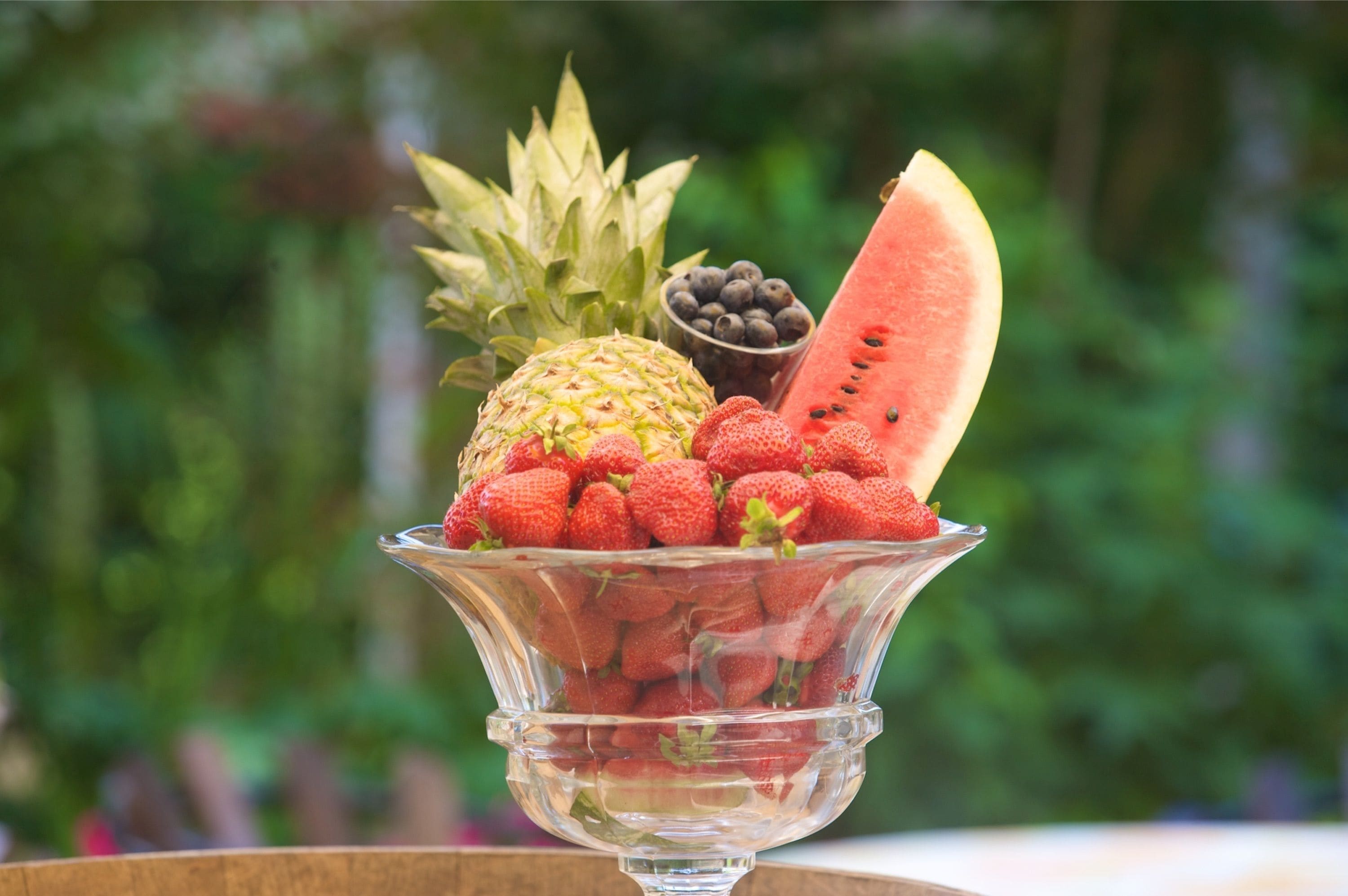 A glass bowl filled with strawberries, a pineapple, and a slice of watermelon.