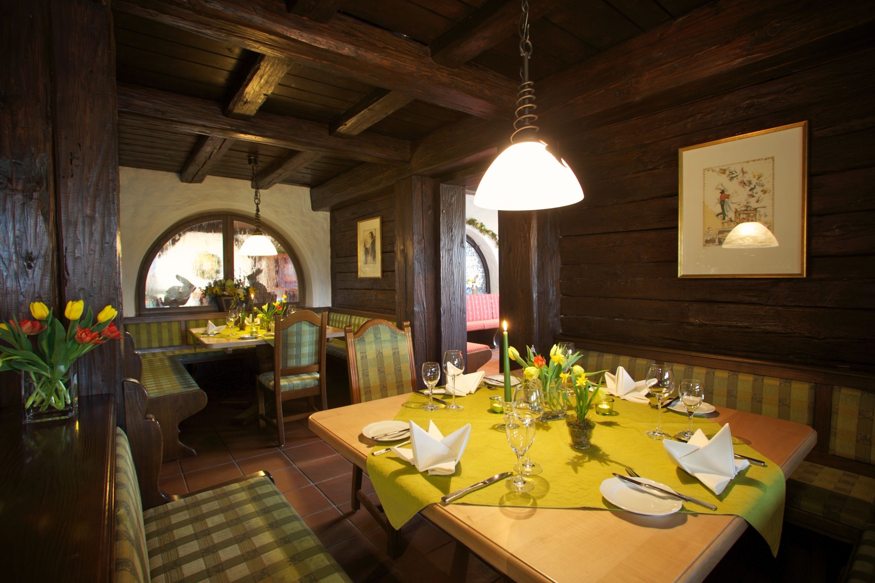 Un comedor con una mesa de madera dispuesta para dos, una lámpara colgante y un cuadro en la pared.