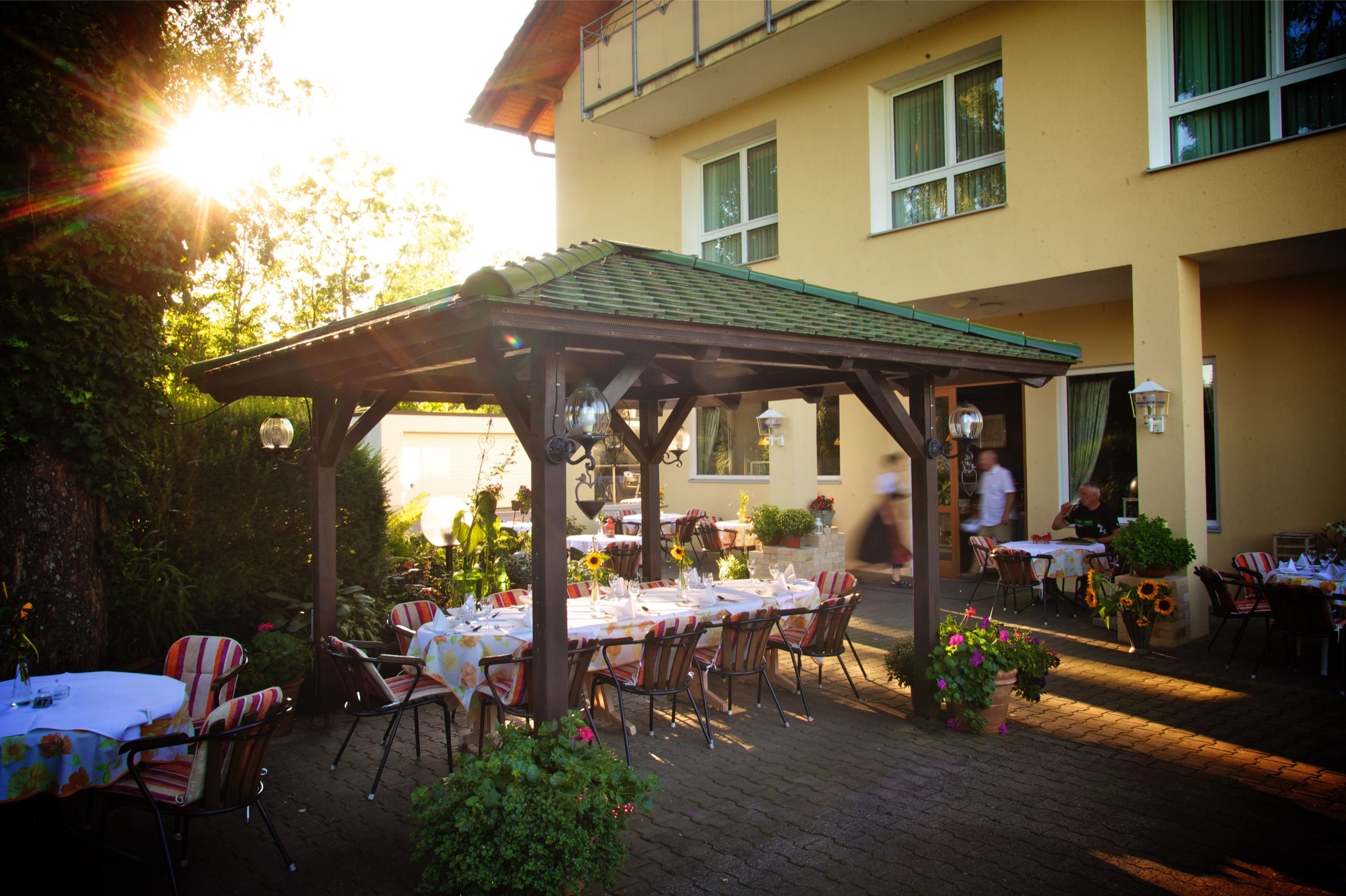 Un patio al aire libre con mesas y sillas, una pérgola y un edificio al fondo.