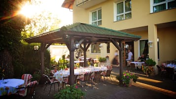Un patio al aire libre con mesas y sillas, una pérgola y un edificio al fondo.