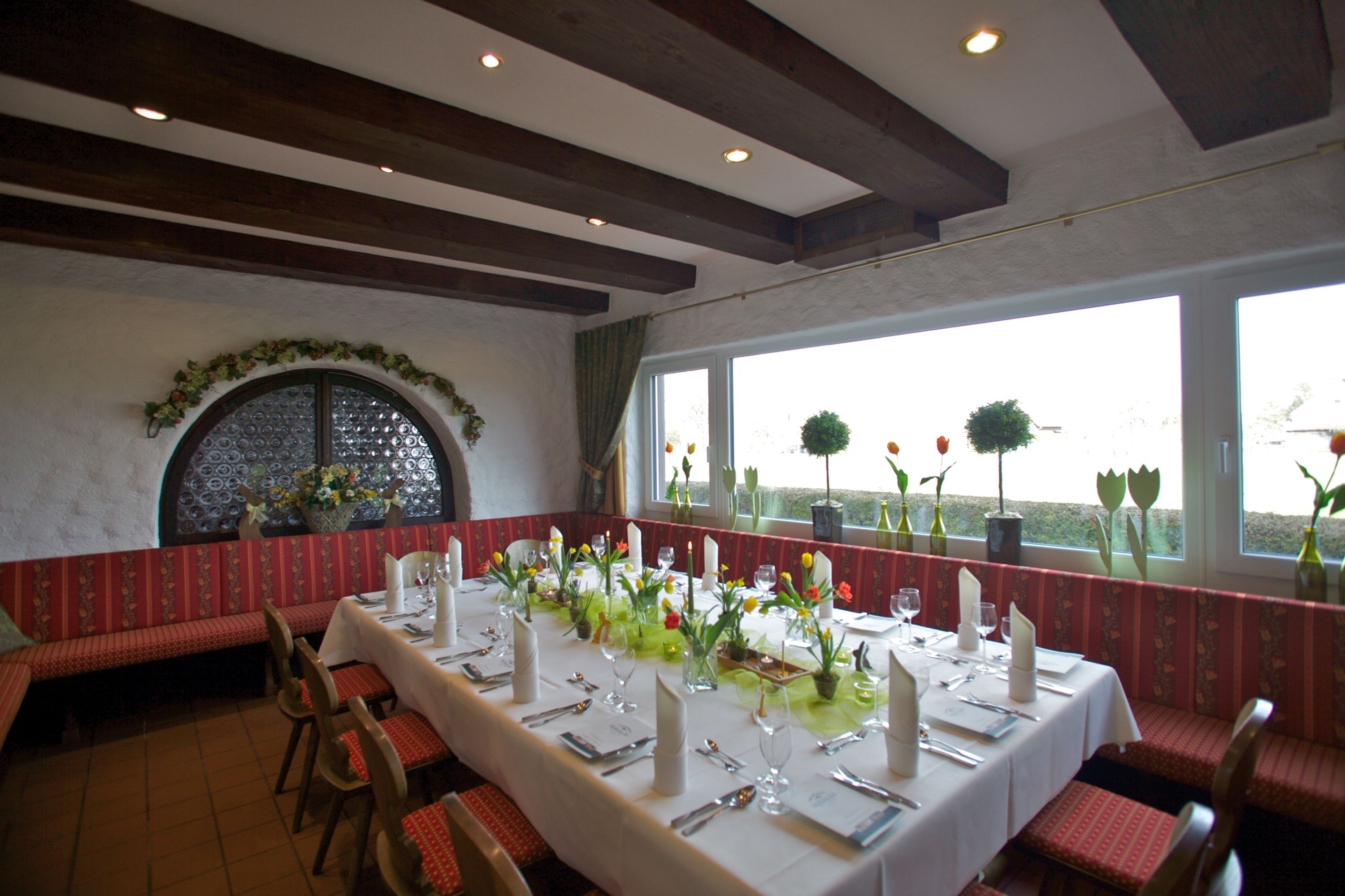 A dining area with a long table set for a meal, benches along the walls, and large windows with views of the outdoors.