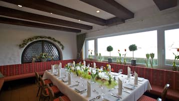 A dining area with a long table set for a meal, benches along the walls, and large windows with views of the outdoors.