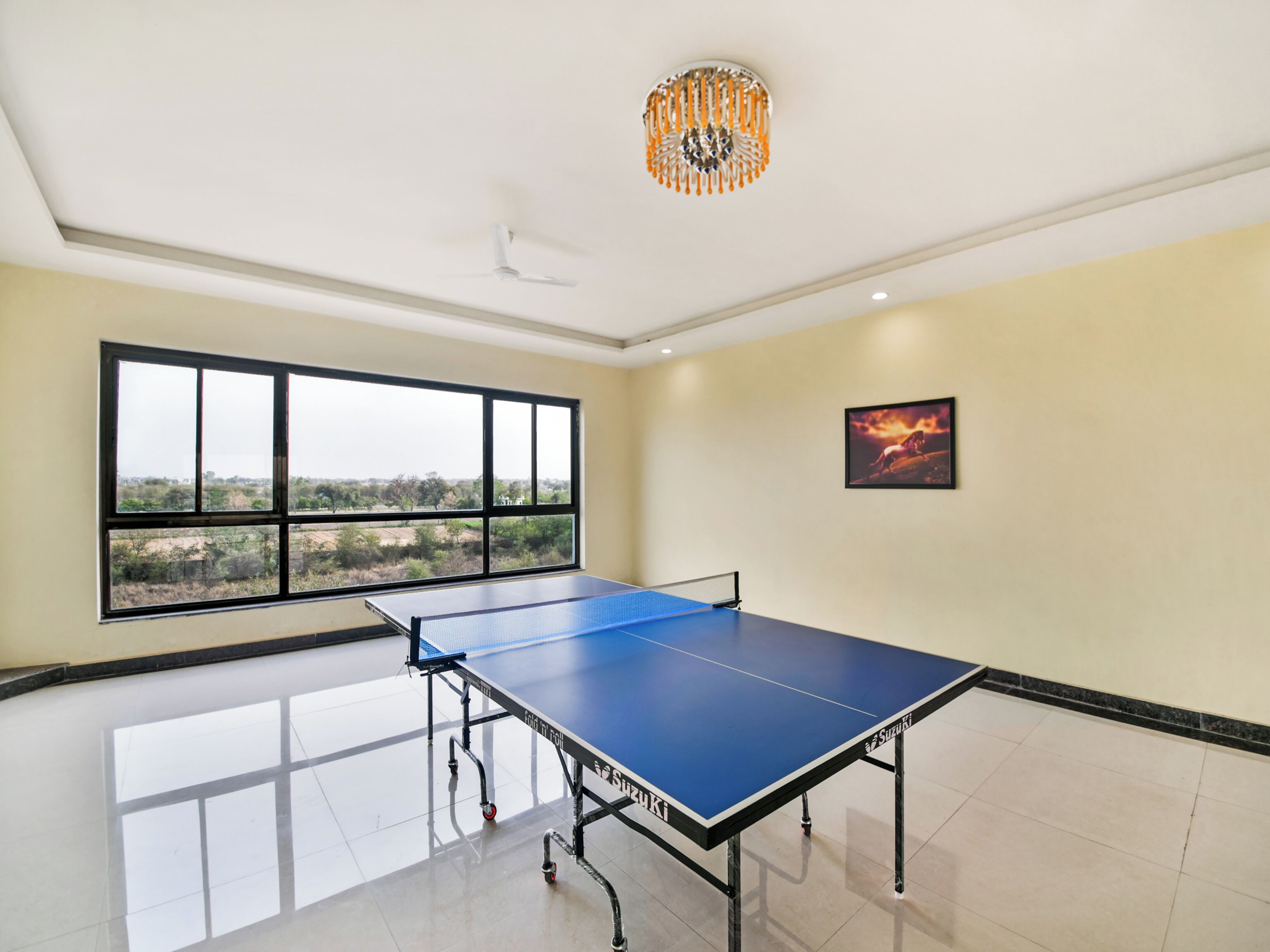 A ping pong table in a room with a large window, a chandelier, and a framed picture on the wall.