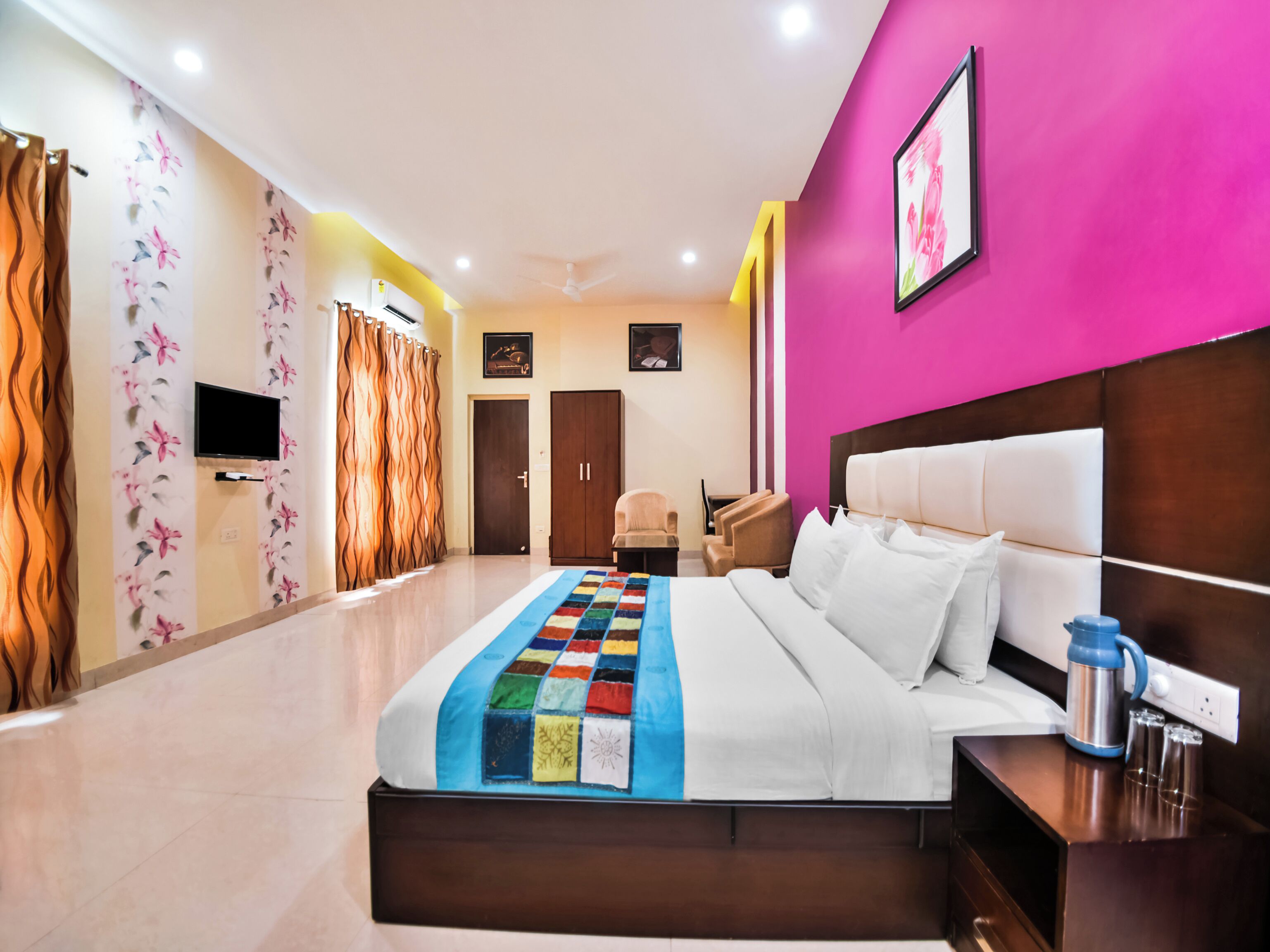A modern hotel room with a large bed, a flat-screen TV, a wardrobe, a desk, and a chair.