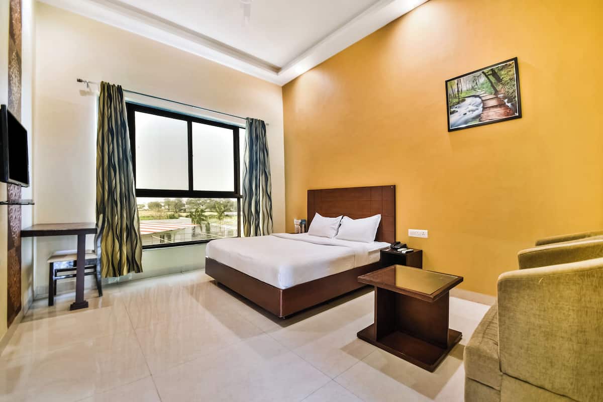 Una habitación de hotel con cama, escritorio, silla y ventana con cortinas.