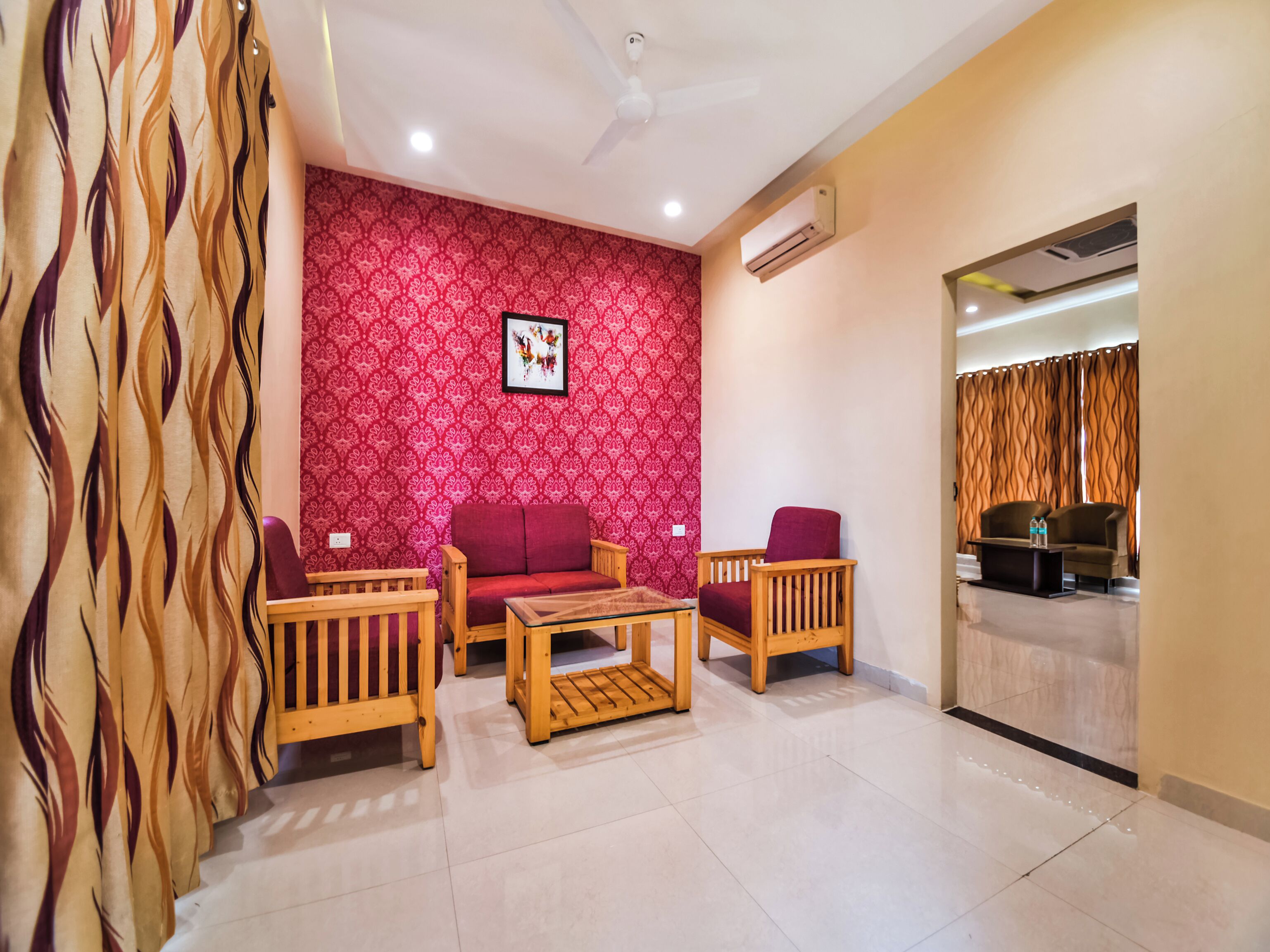 A living room with a red patterned wall, a ceiling fan, and a view into another room through a glass partition.