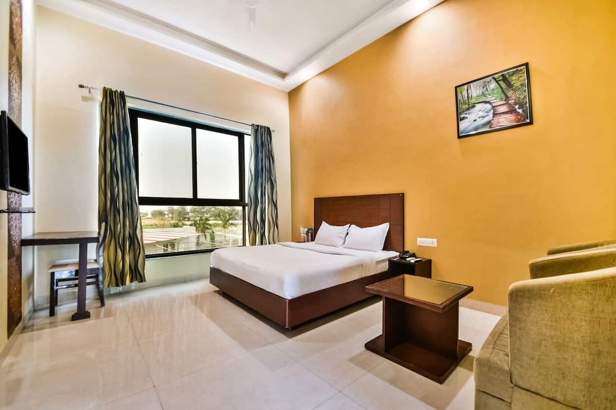 Una habitación de hotel con cama, escritorio, silla, mesita de noche y ventana con cortinas.