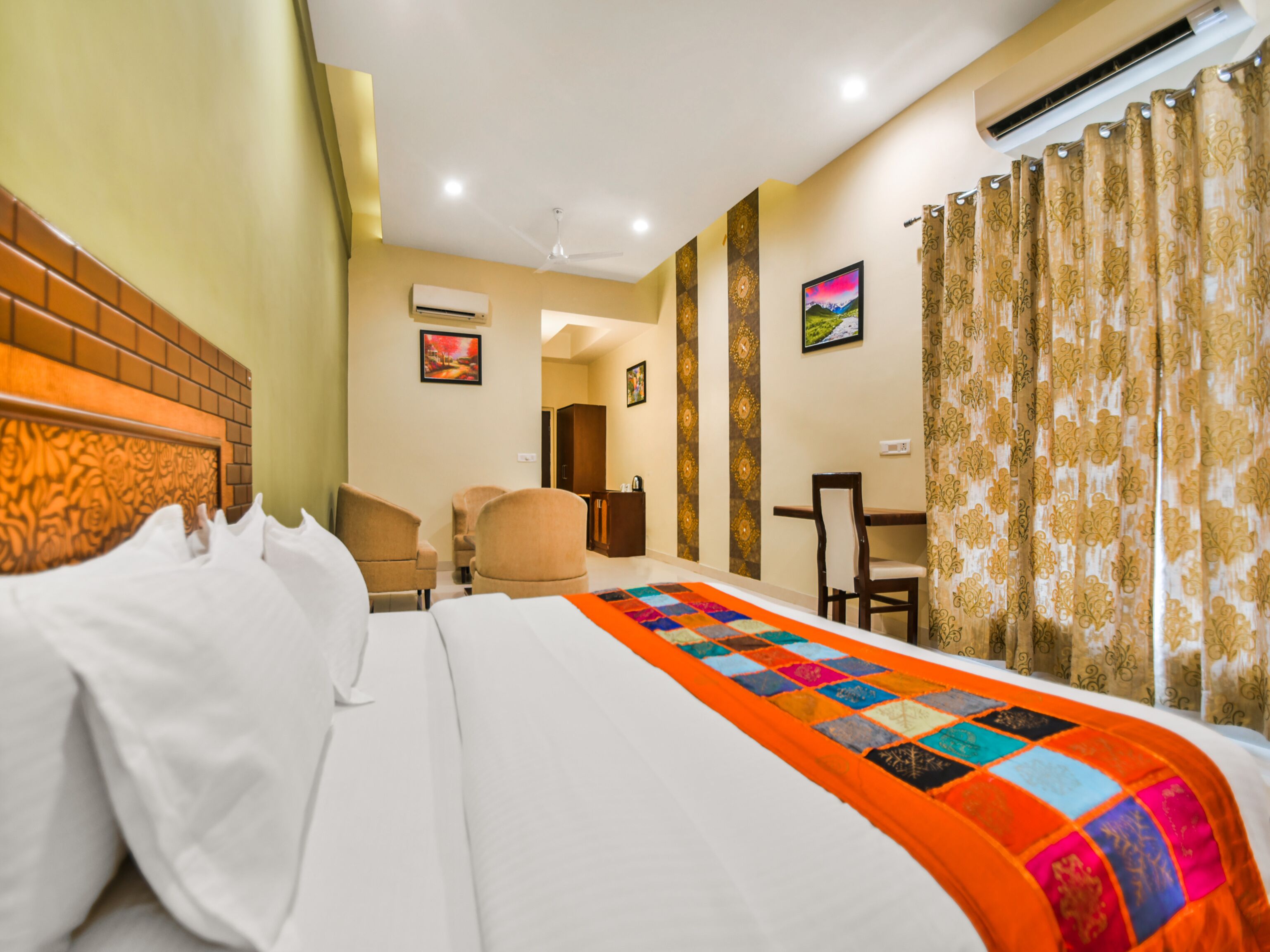 Quarto de hotel com cama, duas cadeiras, escrivaninha e painel decorativo na parede com obras de arte.