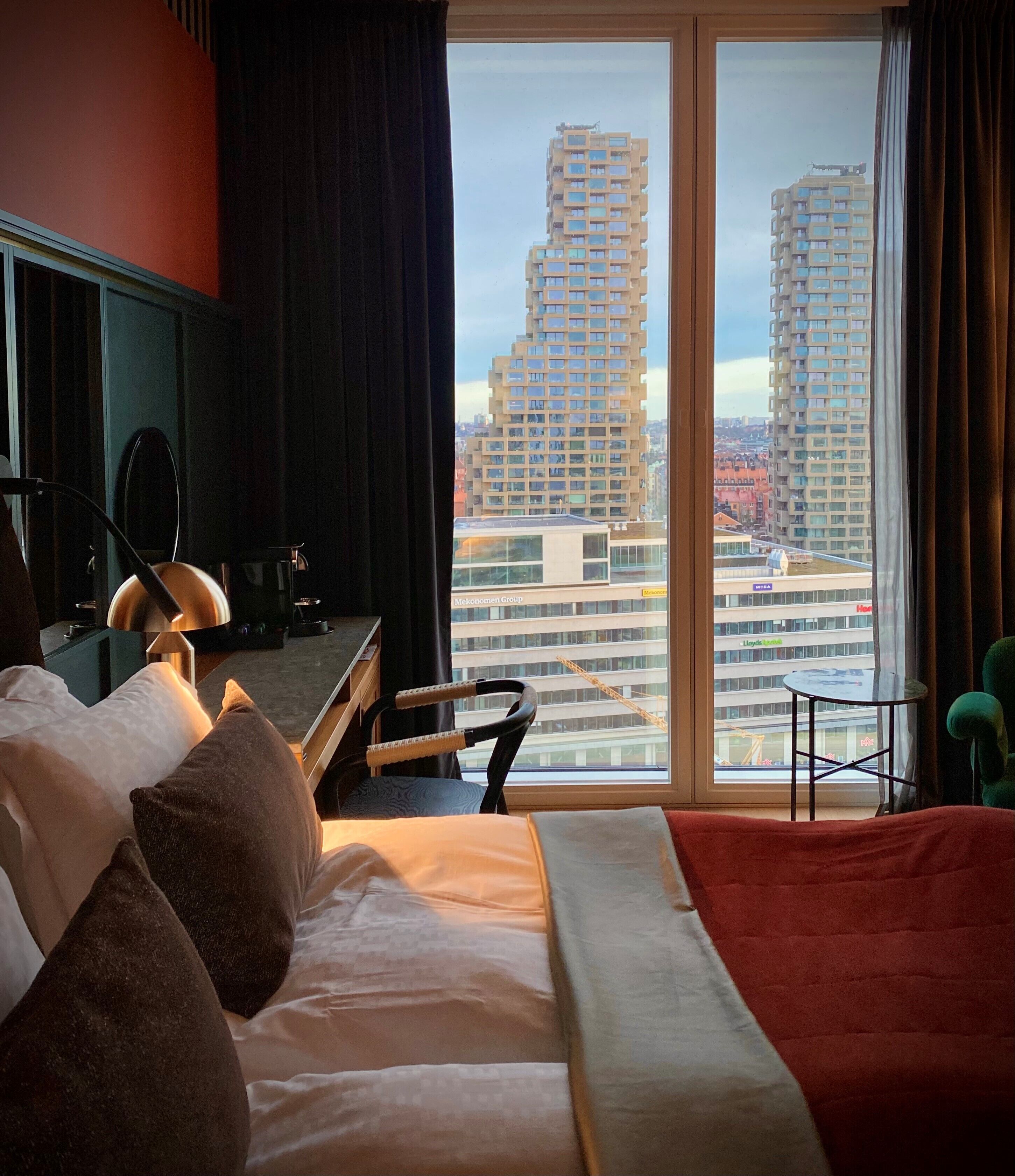 A hotel room with a bed, a desk, a chair, and a view of tall buildings.