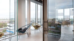 Een ruim balkon met grote ramen en uitzicht op de stad, moderne stoelen en een kleine tafel.