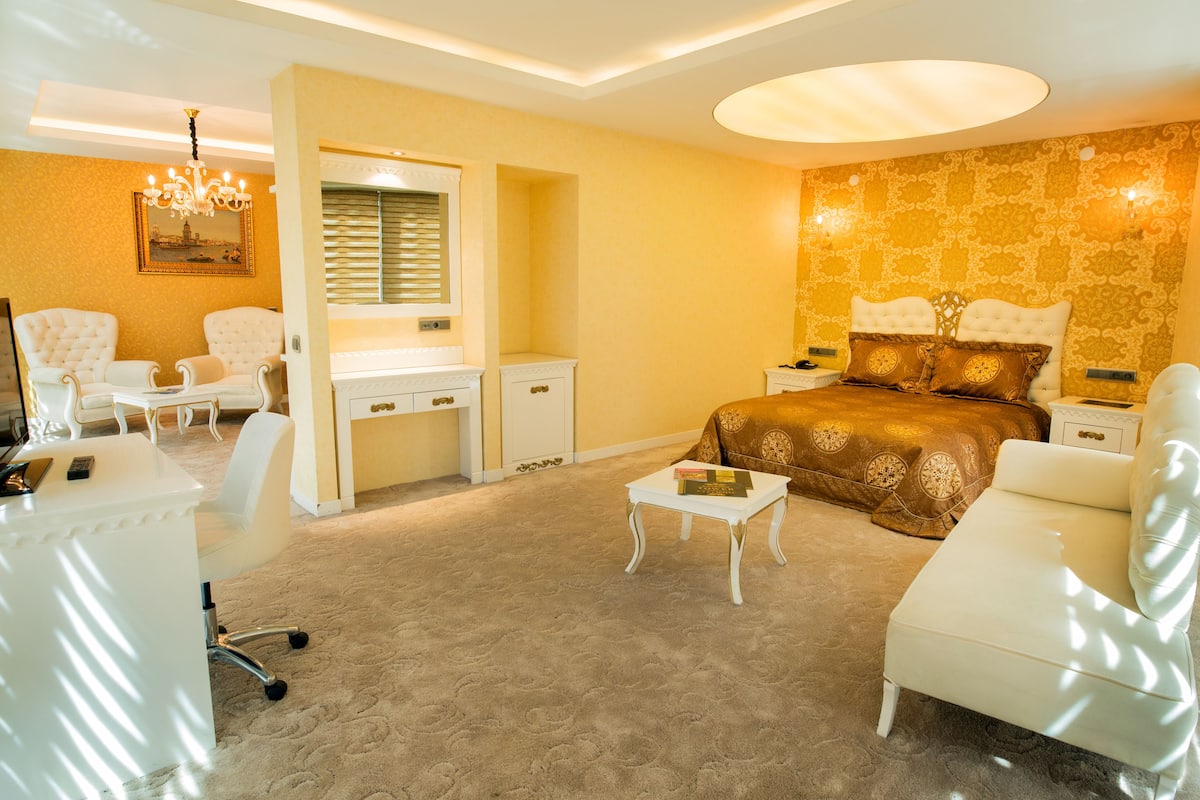 A bedroom with a bed, two chairs, a desk, a small table, and a chandelier.