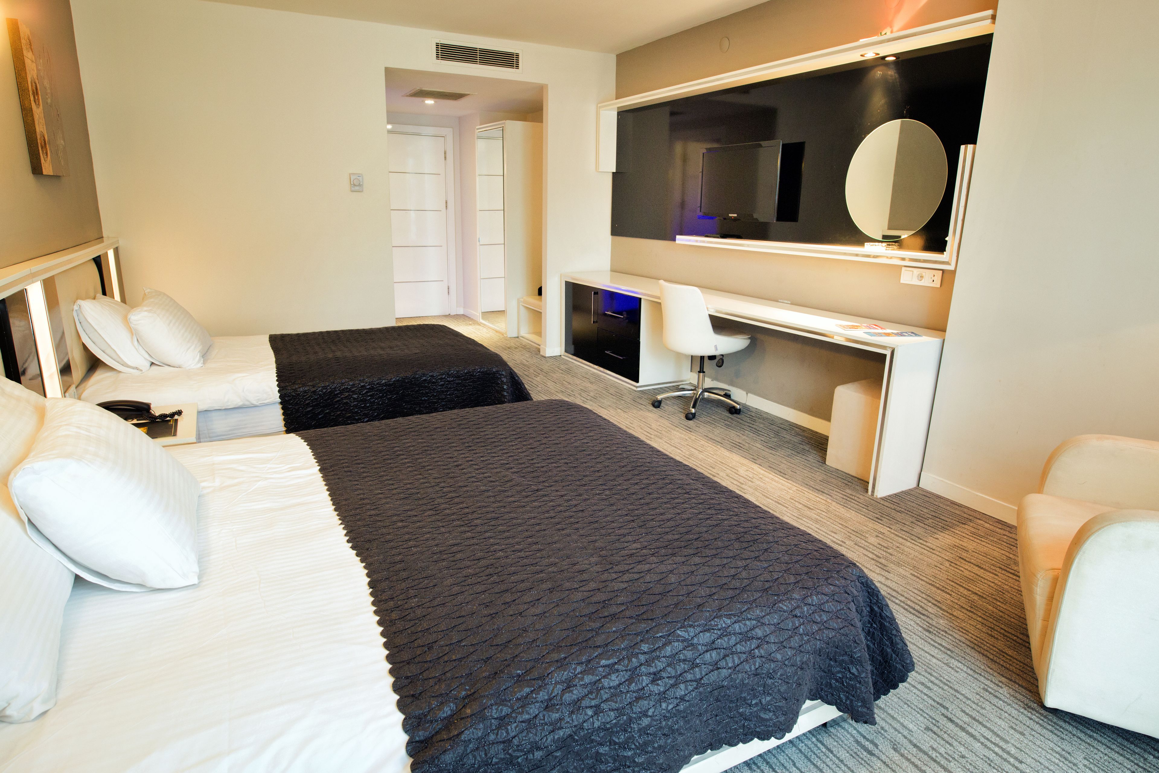 A hotel room with two beds, a desk, a chair, a TV, and a mirror.